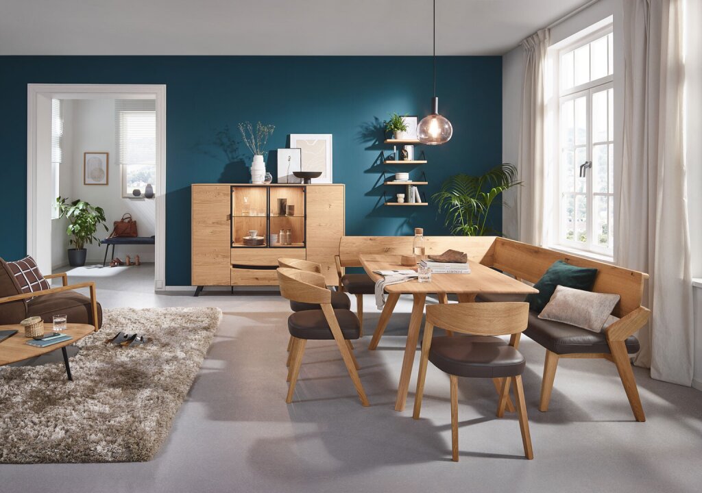Eine harmonische Sitzgruppe aus Eiche Massiv. Freistehende Eckbank mit braunem Naturlederpolsterbezug, drei Stühle mit Holzlehne und gepolstertem Sitzteil, ebenfalls braunes Leder und ein Massivholztisch.