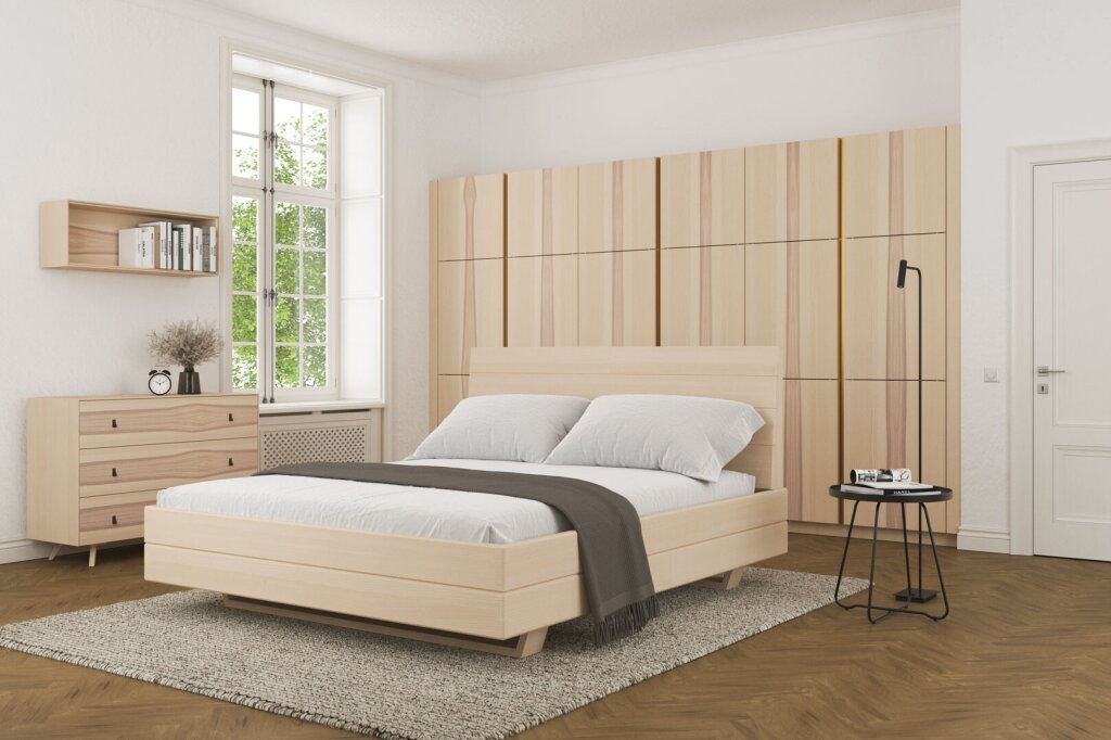 Ein helles Massivholzbett aus Esche mit klaren Linien und reduzierter Formensprache. Das Bett verleiht dem Raum Leichtigkeit und Ruhe, kombiniert mit heller Wandfarbe, großen Fenstern und schlichter Einrichtung. Die Atmosphäre ist freundlich, luftig und modern.
