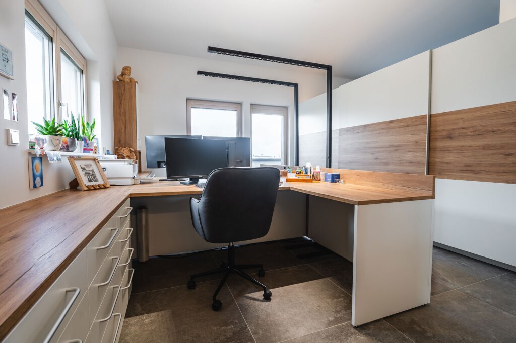 Maßgefertigtes Büro für zwei Personen mit durchgehender Holzarbeitsfläche, viel Stauraum und ergonomischem Arbeitsplatz – vom Tischler geplant für effizientes Arbeiten im Team.