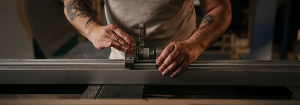 Nahaufnahme der Hände eines Tischlers, der an einer Kreissäge eine präzise Einstellung vornimmt. Das Bild symbolisiert die handwerkliche Sorgfalt und Qualität, die den Preis eines Tischlermöbels bestimmen.