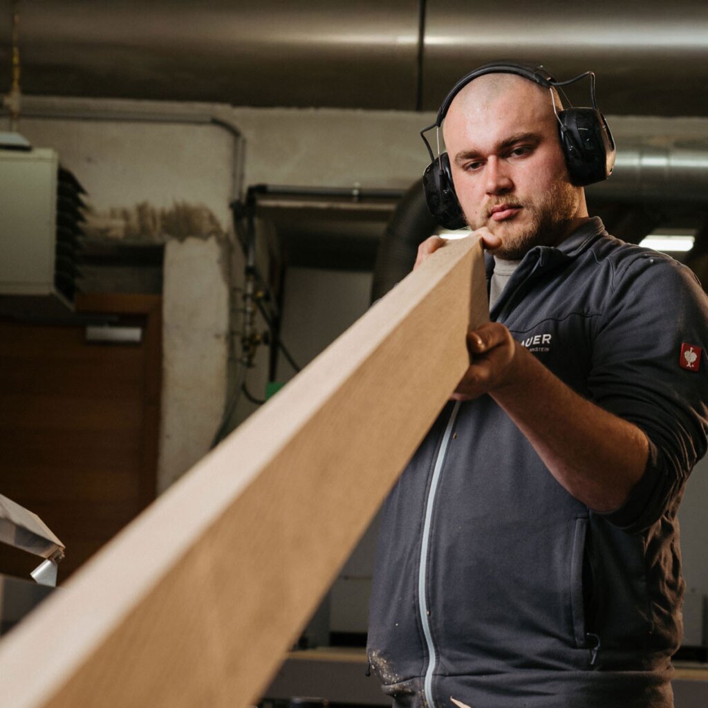 Tischler Paul prüft ein Massivholzbrett, dass er gerade an der Hobelbank abgerichtet hat.