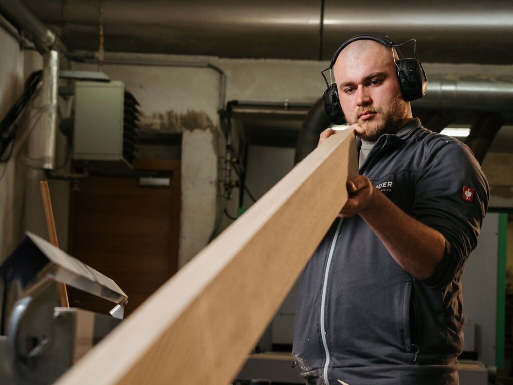 Tischler Paul prüft ein Massivholzbrett, dass er gerade an der Hobelbank abgerichtet hat.