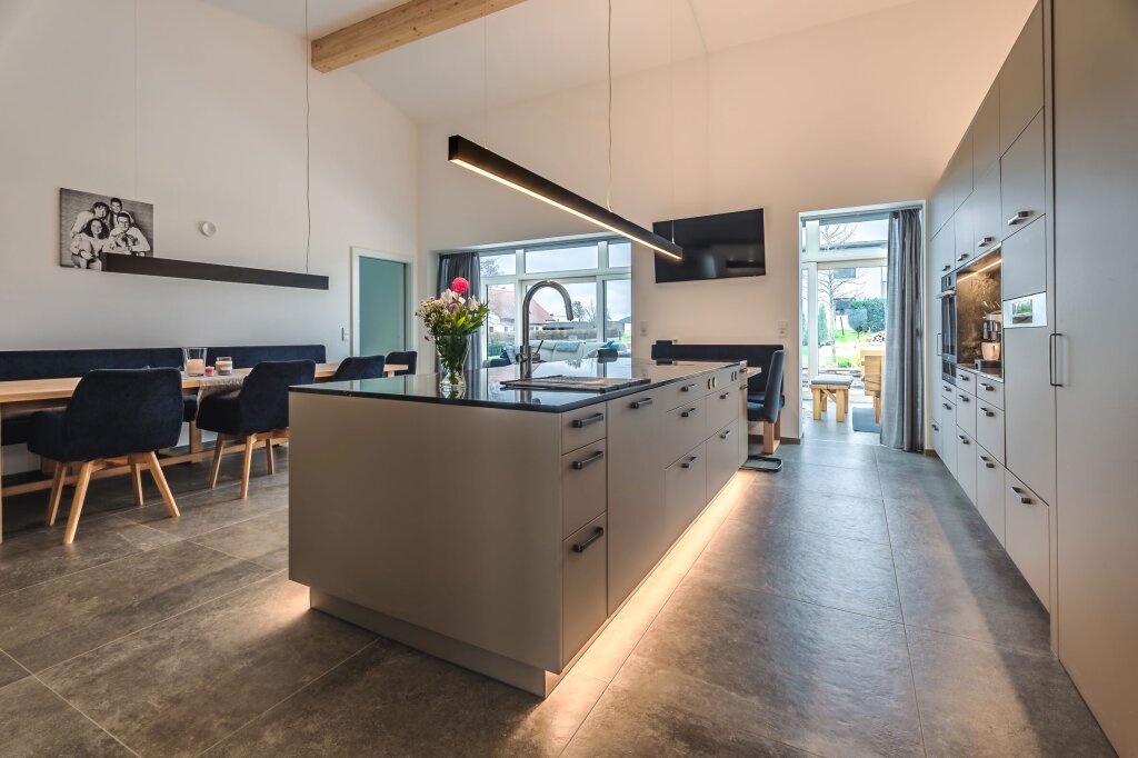 Großzügige Maßküche mit Kochinsel, integrierter Beleuchtung und direktem Zugang zum Garten. Offenes Raumkonzept mit viel Tageslicht und Wohnlichkeit.