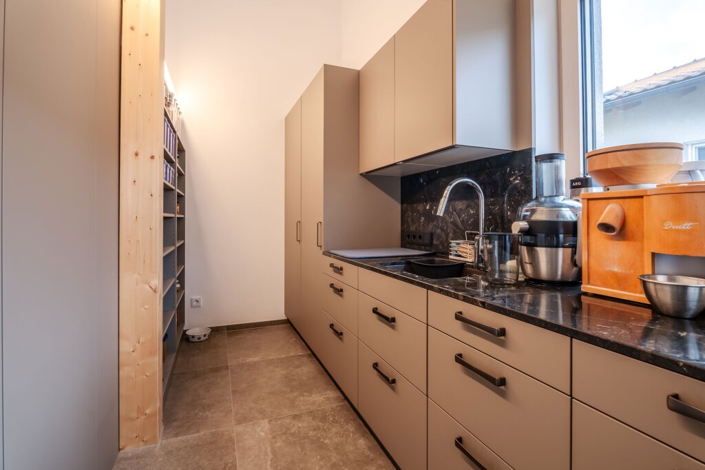 Praktische Hinterküche mit viel Stauraum, modernen Schrankfronten und zusätzlicher Arbeitsfläche. Perfekt für Vorräte, Küchenmaschinen und die Entlastung der Hauptküche.