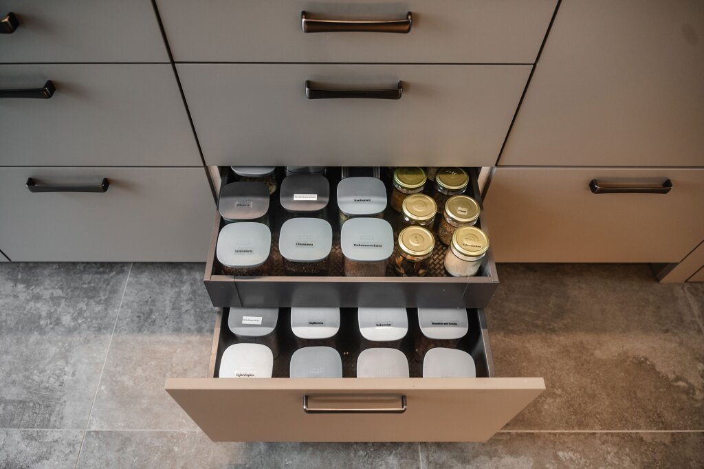 Praktische Auszugslade in einer modernen Maßküche – Gewürze, Hülsenfrüchte und Vorräte sind übersichtlich in beschrifteten Dosen und Gläsern verstaut. Durchdachte Stauraumlösungen vom Tischler sorgen für Ordnung, Übersicht und Alltagstauglichkeit.