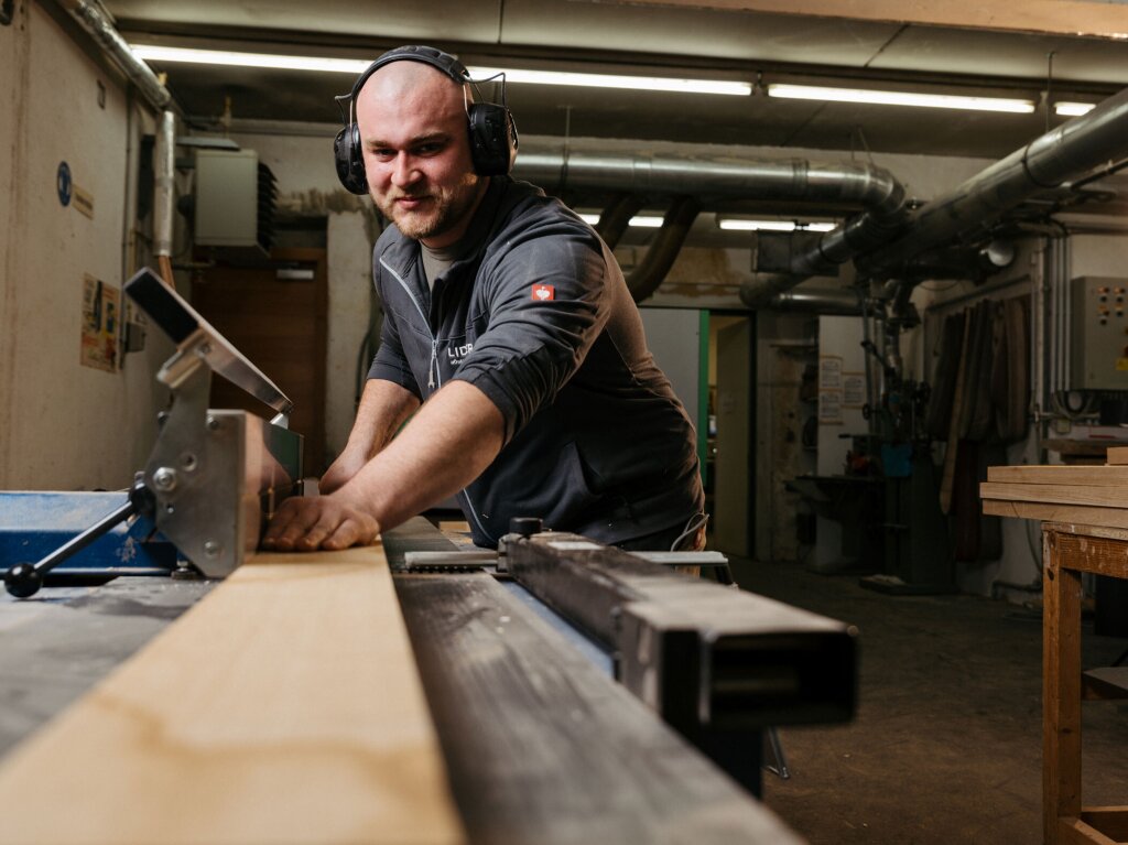Tischler Arbeitet an der Abricht- Maschine. Er trägt einen Gehörschutz.