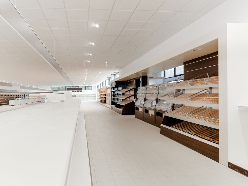 Weitwinkelaufnahme eines Lebensmittelladens. Rechts sieht man die Backabteilung mit Regalen für Gebäck, links sind leere Regalflächen zu sehen.